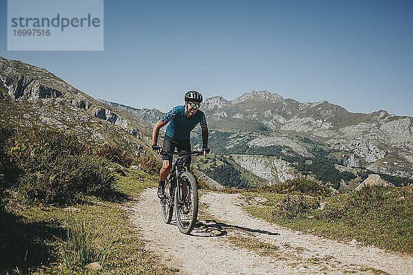 Männlicher Radfahrer fährt Mountainbike auf einem Weg gegen den Himmel  Nationalpark Picos de Europa  Asturien  Spanien
