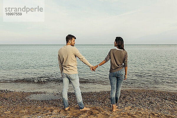 Junge Freundin und Freund halten Hände am Strand