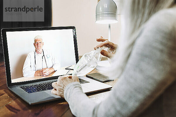 Ältere Frau zeigt dem Arzt eine medizinische Probe per Videoanruf zu Hause