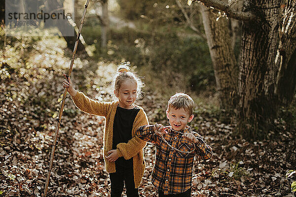 Mädchen und Junge spielen mit Stock und Seil im Herbst im Wald stehend