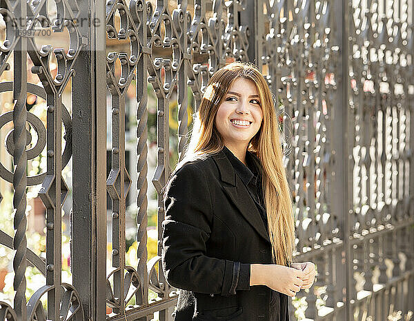 Junge Frau lächelt  während sie vor einem Tor steht