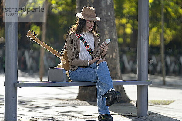 Junge Frau benutzt ihr Smartphone an der Bushaltestelle
