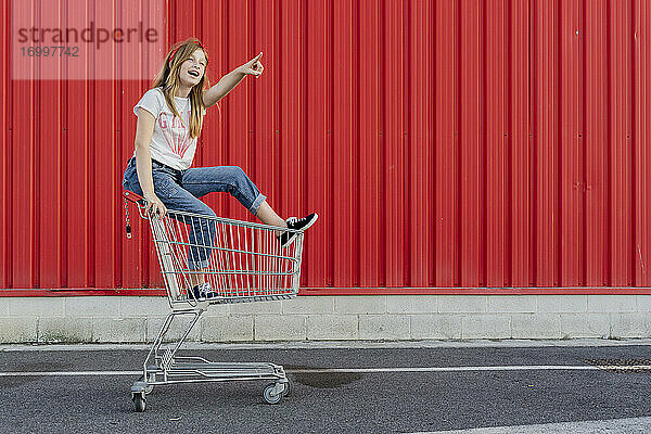 Mädchen in einem Einkaufswagen vor einer roten Wand