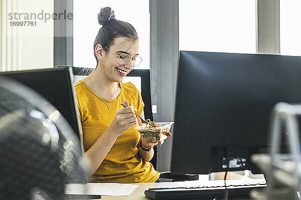 Lächelnde Geschäftsfrau beim Essen im Büro sitzend