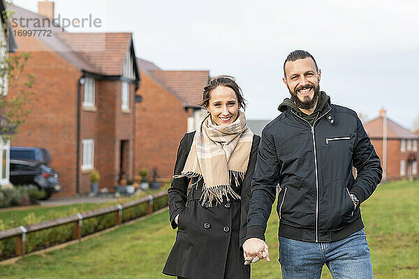 Lächelndes Paar hält sich an den Händen  während es vor seinem neuen Haus steht