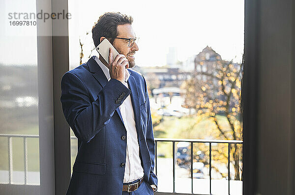 Älterer Geschäftsmann  der auf einem Balkon im Büro steht und mit seinem Handy telefoniert