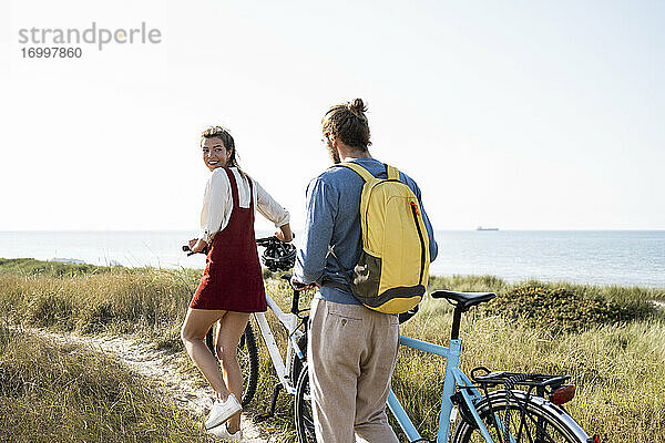 Junger Mann und Frau mit Fahrrädern auf dem Fußweg gegen den klaren Himmel