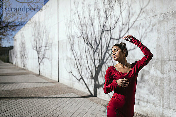 Frau in rotem Kleid mit Tänzerin Pose und Baum Schatten an der Wand