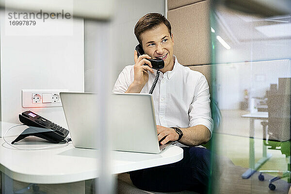 Geschäftsmann lächelnd beim Telefonieren im Büro sitzend