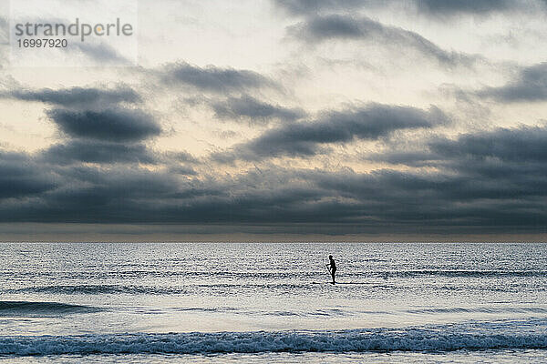 Weibliche Paddleboarderin surft in der Morgendämmerung auf dem Meer