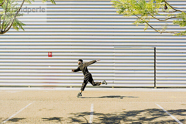 Mann in schwarzem Overall springt vor einem Industriegebäude in die Luft