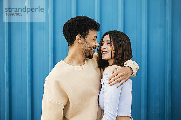 Lächelnder junger Mann  der eine Frau umarmt  während er an einer blauen Wand steht