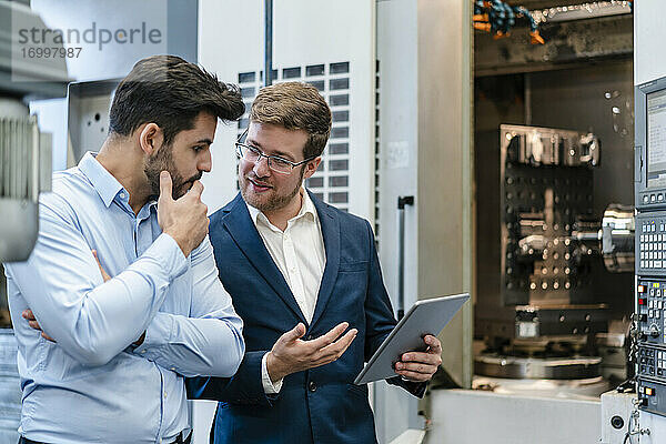 Geschäftsmann mit männlichem Kollegen diskutiert  während er ein digitales Tablet in der Industrie hält