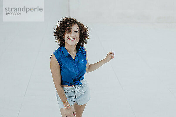Lächelnde Frau mit lockigem Haar steht auf dem Boden vor einer gefliesten Wand