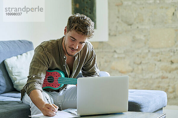 Mann lernt Ukulele über Laptop während eines Online-Tutorials zu Hause