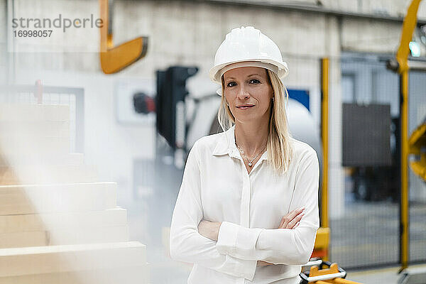Selbstbewusste Geschäftsfrau mit Schutzhelm in einer Fabrik stehend