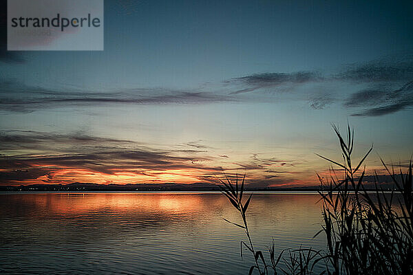 Malerischer Blick auf den See vor einem dramatischen Himmel bei Sonnenuntergang
