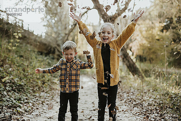 Glückliches Geschwisterkind  das im Herbst im Wald steht und mit einem trockenen gefallenen Blatt spielt