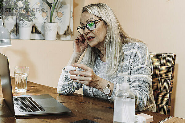 Ältere Frau trägt drahtlose In-Ear-Kopfhörer während einer Online-Beratung zu Hause
