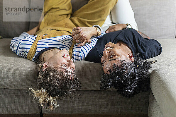 Lesbisches Paar hält sich an den Händen  während es zu Hause auf dem Sofa liegt