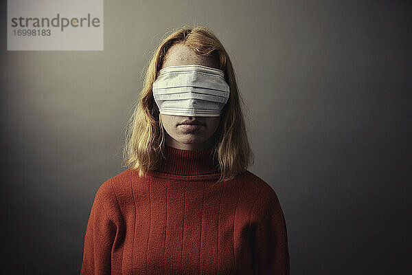 Teenager-Mädchen trägt eine Schutzmaske auf den Augen und steht vor einem grauen Hintergrund