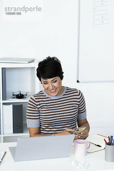 Porträt einer Geschäftsfrau  die am Schreibtisch sitzt und ihr Smartphone in der Hand hält