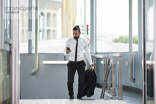Geschäftsmann geht mit Smartphone in der Hand eine Treppe hinauf
