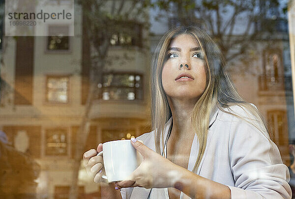 Junge schöne Frau hält Kaffeetasse beim Sitzen im Café