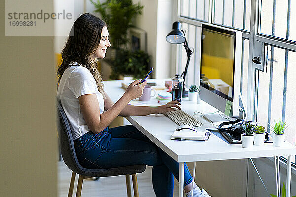 Lächelnde Geschäftsfrau  die ein Smartphone benutzt  während sie im Büro sitzt