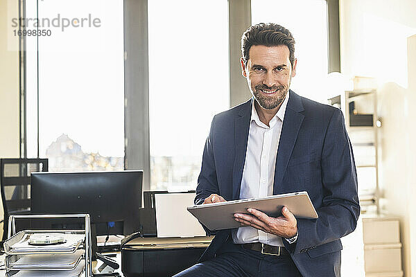 Lächelnder Geschäftsmann  der ein digitales Tablet benutzt  während er im Büro sitzt