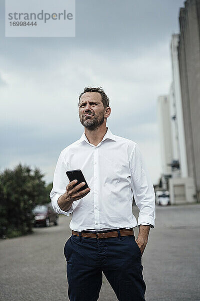 Männlicher Unternehmer  der ein Smartphone hält  während er auf der Straße steht