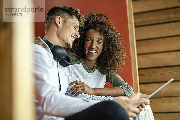 Glücklicher Mann mit digitalem Tablet  der bei einer fröhlichen Frau zu Hause sitzt