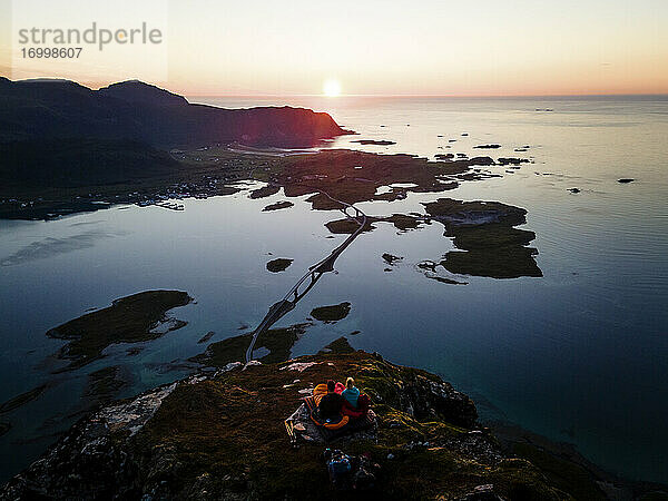 Erwachsener Mann und Frau bewundern die Aussicht  während sie auf einem Berg bei Volandstinden  Lofoten  Norwegen  sitzen