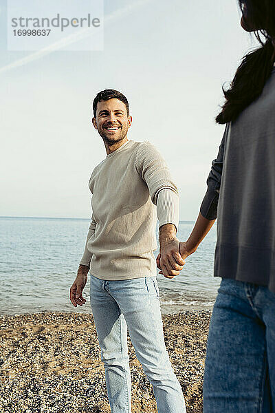 Lächelnder Mann  der die Hand einer Frau hält  während er am Strand steht