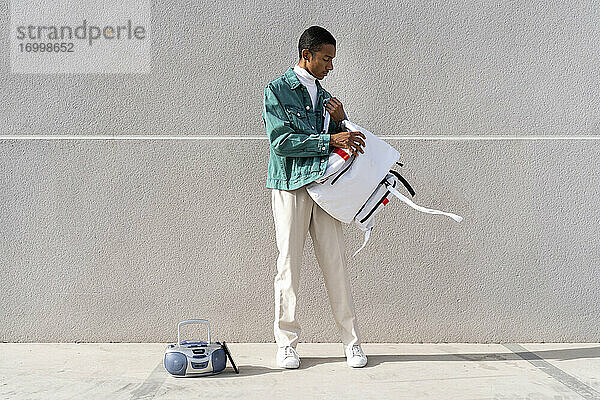 Mann nimmt eine Tasche ab  während er vor einer grauen Wand mit einem Radio steht