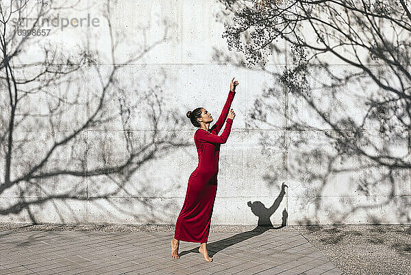 Frau in rotem Kleid mit Tänzerin Pose und Baum Schatten an der Wand