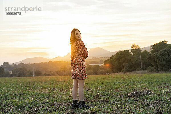 Glückliche junge Frau  die bei Sonnenuntergang auf dem Lande steht