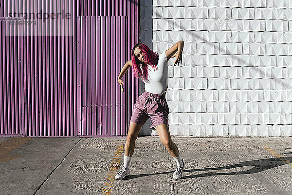 Junge Frau mit gefärbten roten Haaren tanzt vor einer lila Wand in der Stadt