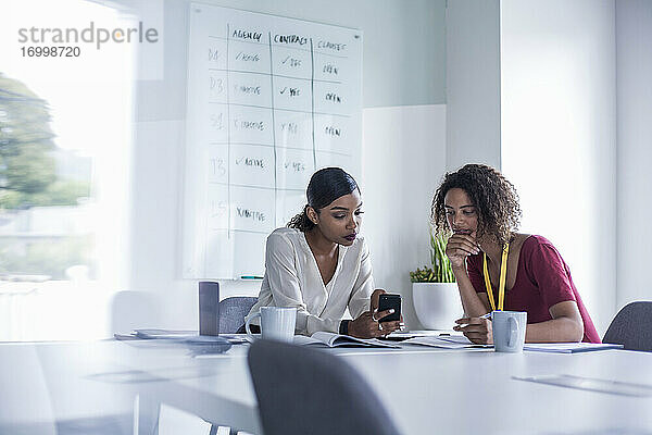 Weibliche Kollegen benutzen ihr Smartphone  während sie am Schreibtisch im Büro sitzen