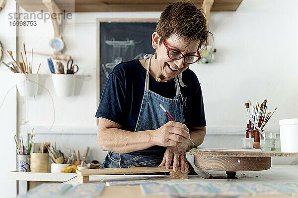 Lächelnde Besitzerin beim Bemalen von Handwerksprodukten in der Keramikwerkstatt
