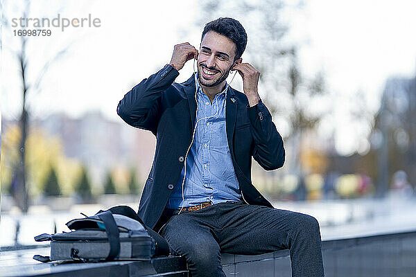 Lächelnder Geschäftsmann mit Kopfhörern  der auf einer Bank sitzt