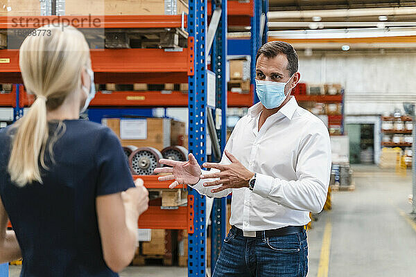 Geschäftsmann im Gespräch mit einer Kollegin in einer Fabrik während COVID-19