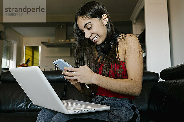 Teenager-Mädchen mit Laptop und Handy  während sie zu Hause auf dem Sofa sitzt