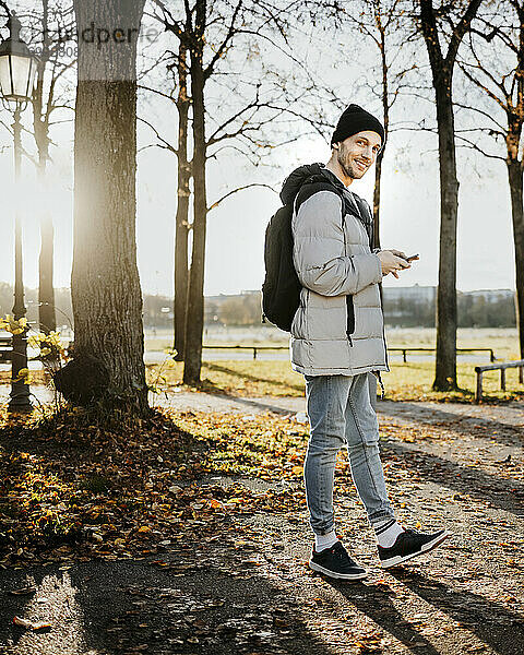 Mann hält Smartphone während eines Herbstspaziergangs im Park