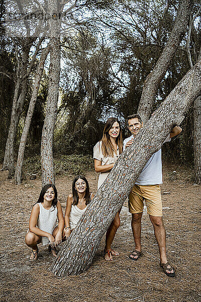 Mutter und Vater mit Töchtern hinter einem Baumstamm im Wald