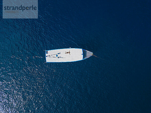Luftaufnahme eines Mannes ohne Hemd  der sich auf dem Dach eines Bootes entspannt  das im blauen Wasser des Arabischen Meeres im Sommer treibt