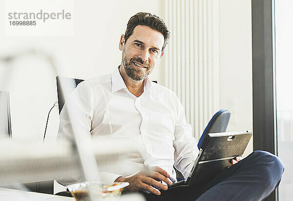 Lächelnder Geschäftsmann mit digitalem Tablet im Büro