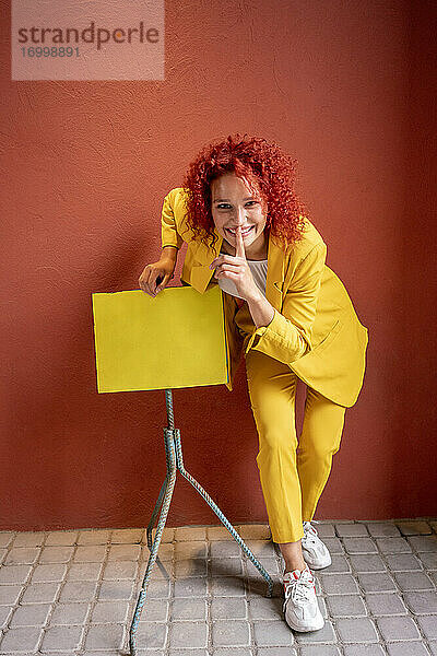 Junge Frau im gelben Anzug  die sich mit dem Finger auf dem Mund an einen Notenständer lehnt