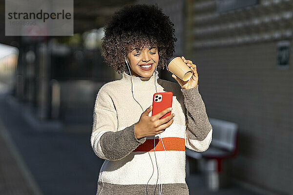 Lächelnde junge Frau macht Selfie mit wiederverwendbarem Becher am Bahnhof