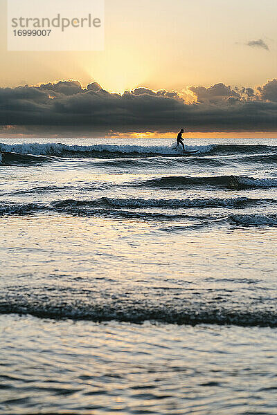 Silhouette Mann Surfen mit Paddleboard auf dem Meer gegen den Himmel in der Morgendämmerung